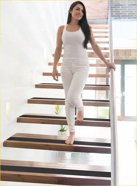 Woman dressed in white walking down a flight of slippery wooden stairs with anti-slip stair grip tape on the end of each stair