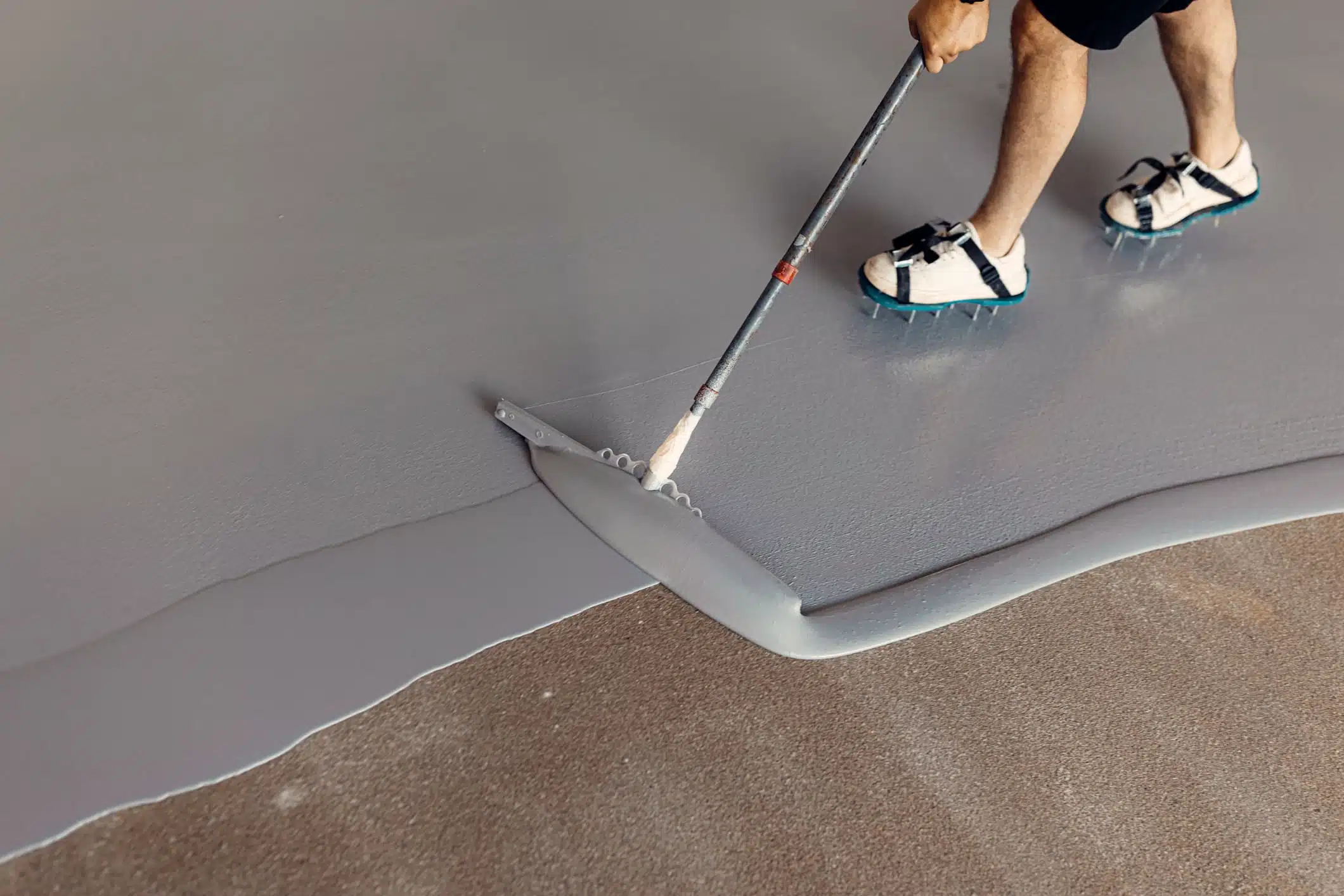 Grey Floor coating by Slip No More being rolled onto a floor by a man with spikes on shoes